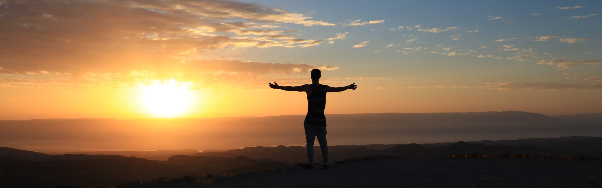 Person standing with outstretched arms at sunset